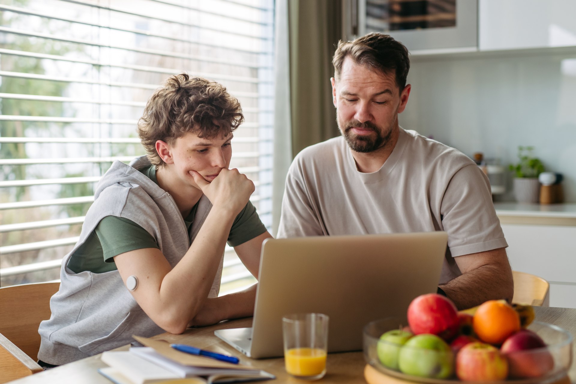 Father helping teenage son with homework on laptop in kitchen
